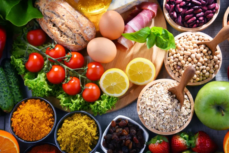 Colorful assortment of healthy foods including vegetables, eggs, beans, oats, fruit, and spices arranged on a table.