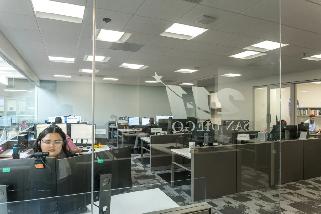 Photo of a modern office seen through a glass wall with a large “211 SAN DIEGO” logo