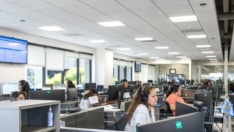 Wide view of an open-plan office with rows of computer stations and several employees wearing headsets while working.