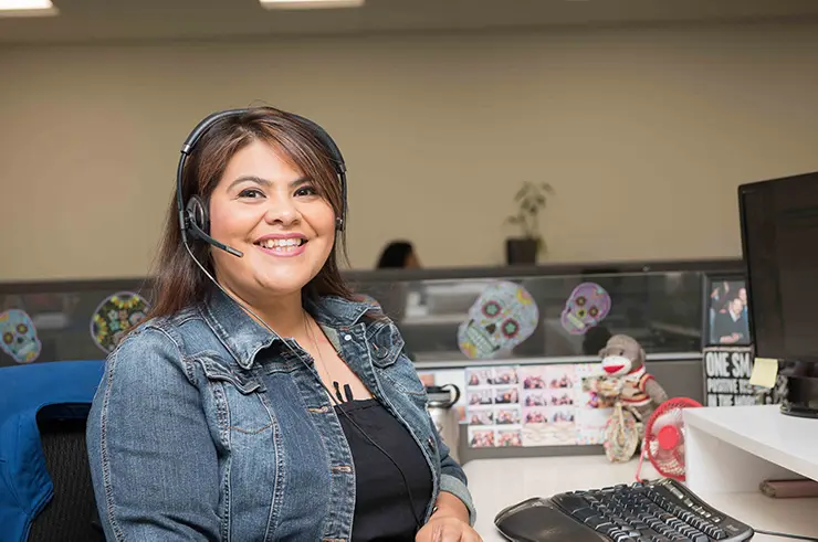 Smiling call center agent wearing a headset and sitting at an office desk with a keyboard and monitor.