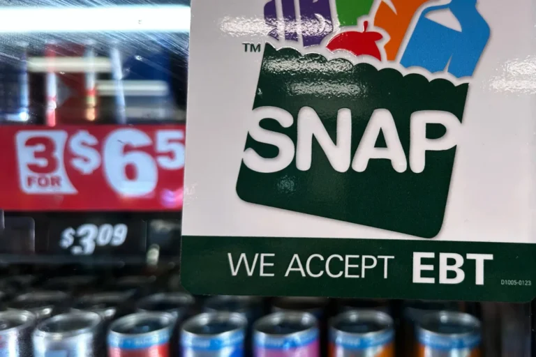 Close-up of a SNAP sign reading “We Accept EBT” on a store cooler door.